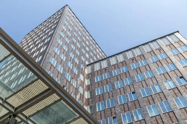 Hoogbouw aan de Barbara Strozzilaan met moderne gevel van baksteen en glas tegen een heldere blauwe lucht.